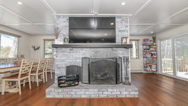 living area with ornamental molding, a brick fireplace, wood-type flooring, and a baseboard heating unit