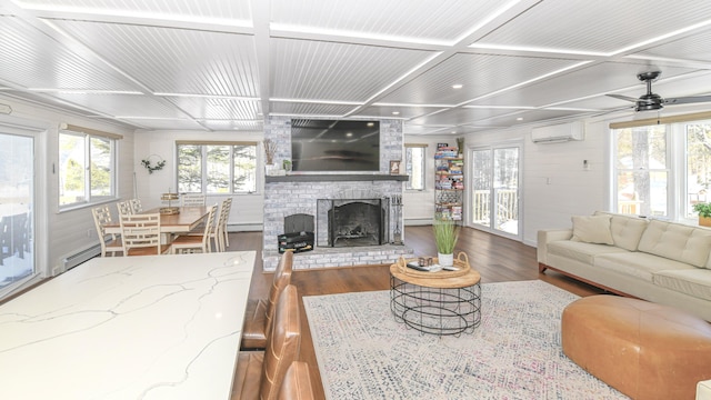 7 Birch Dr, Raymond, ME 04071 - living room with wood finished floors, a baseboard radiator, ceiling fan, a brick fireplace, and a wall unit AC