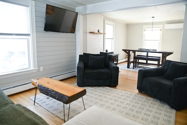 living room featuring light wood finished floors, baseboard heating, a wall mounted AC, ornamental molding, and wood walls