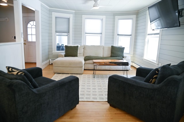 living room featuring ceiling fan, baseboard heating, light wood-style flooring, and crown molding