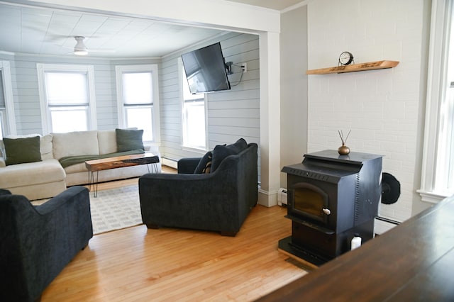 living area featuring ornamental molding, a baseboard radiator, a wood stove, and light wood-style floors