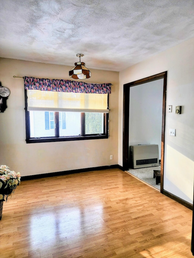 unfurnished room featuring heating unit, a textured ceiling, and wood finished floors