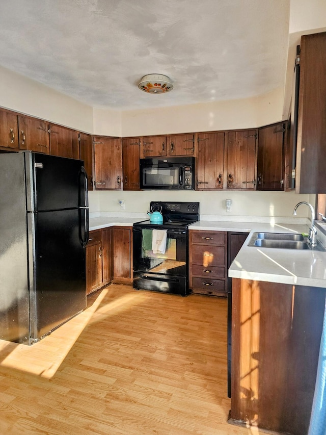 kitchen featuring light wood-style flooring, black appliances, light countertops, and a sink