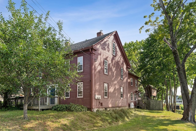 view of side of property featuring a wooden deck, a lawn, and a chimney