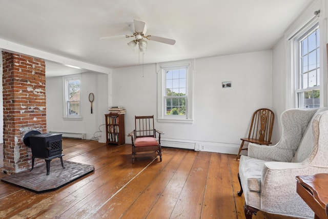 sitting room featuring wood-type flooring, baseboard heating, ceiling fan, and a wood stove