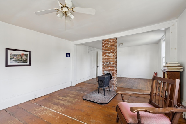 living area with baseboards, a wood stove, ceiling fan, and hardwood / wood-style floors