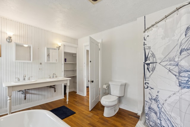 bathroom with baseboards, toilet, double vanity, wood finished floors, and a textured ceiling