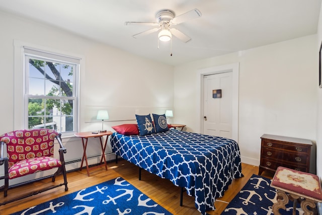 bedroom with ceiling fan, a baseboard radiator, and wood finished floors