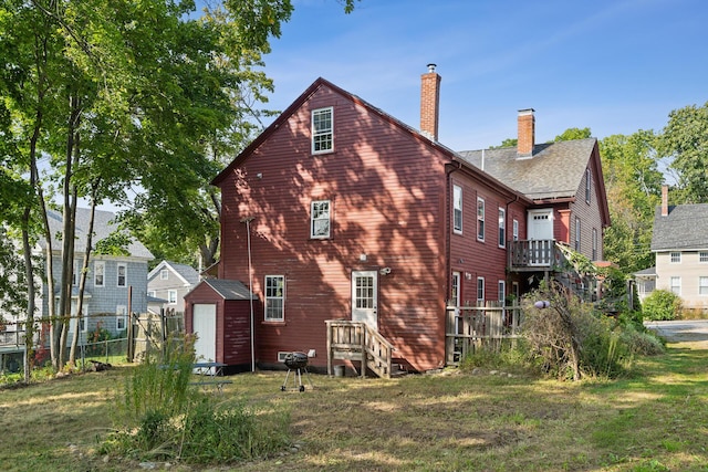 back of property featuring fence, a chimney, a storage shed, a yard, and an outbuilding