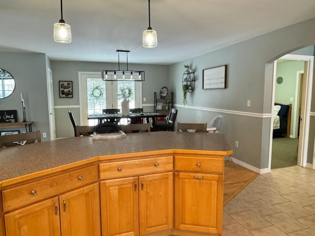 kitchen with brown cabinetry, arched walkways, hanging light fixtures, and light tile patterned floors