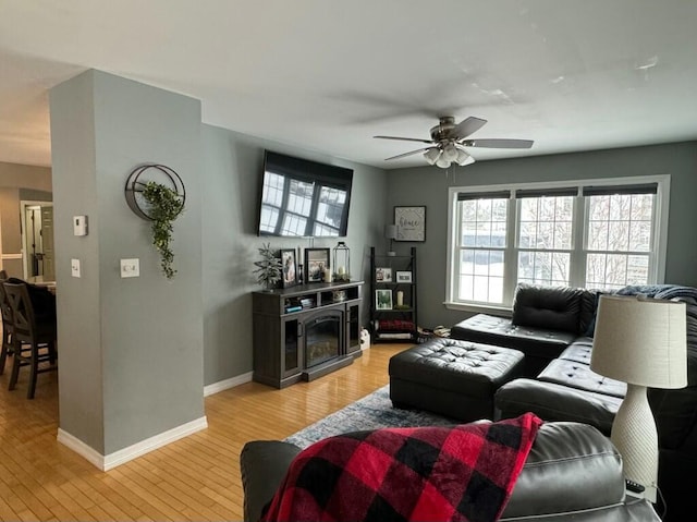 living area with light wood-style floors, a fireplace, baseboards, and ceiling fan