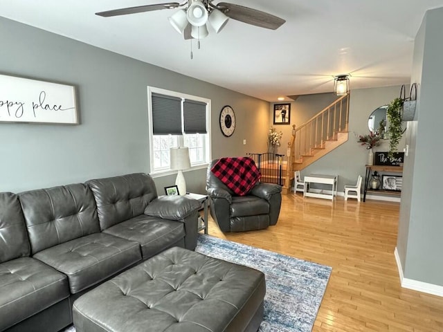 living area with light wood-type flooring, baseboards, stairway, and ceiling fan