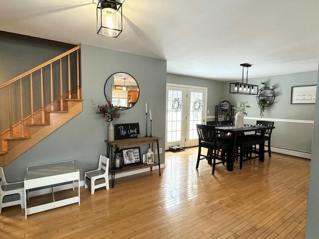 dining area featuring a baseboard radiator, wood-type flooring, stairway, and baseboards