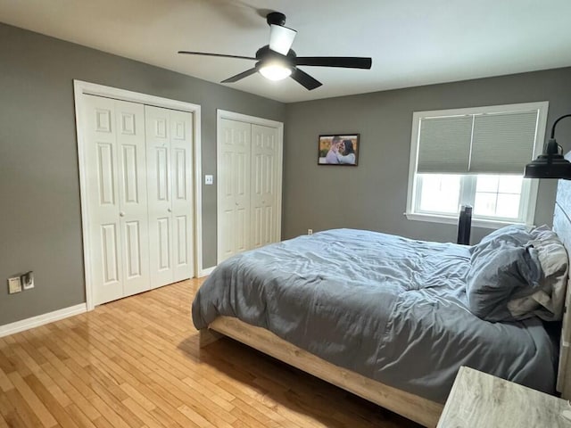 bedroom featuring wood finished floors, two closets, a ceiling fan, and baseboards