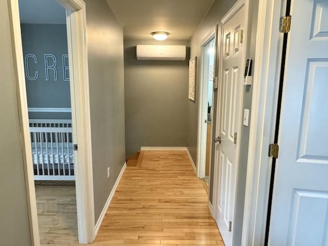 corridor with light wood finished floors, baseboards, and a wall mounted AC