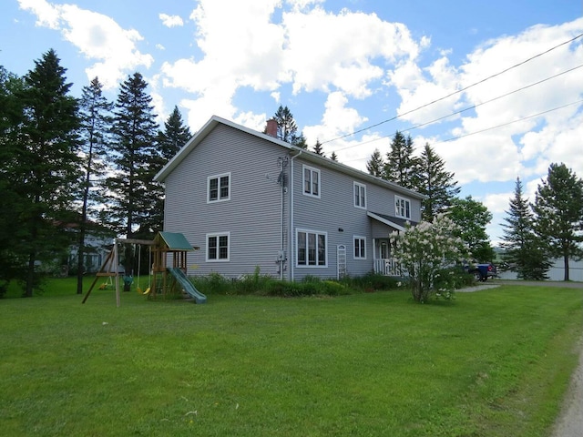 rear view of house featuring a playground, a chimney, and a lawn