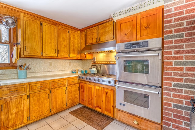 kitchen with light tile patterned floors, decorative backsplash, appliances with stainless steel finishes, light countertops, and under cabinet range hood