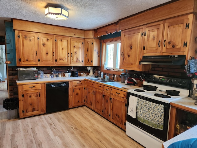 kitchen featuring under cabinet range hood, light countertops, brown cabinets, light wood-style floors, and black appliances