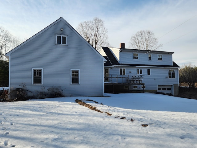 snow covered rear of property with a deck and a chimney