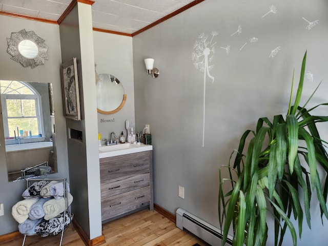 bathroom with vanity, wood finished floors, baseboards, a baseboard radiator, and ornamental molding