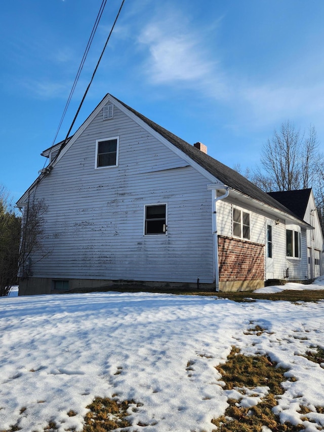 view of snowy exterior featuring brick siding and a chimney