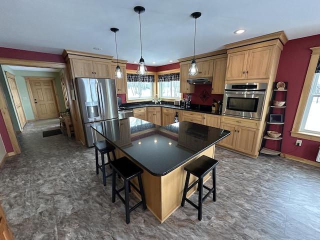 kitchen with dark countertops, a breakfast bar area, stainless steel appliances, under cabinet range hood, and a wealth of natural light