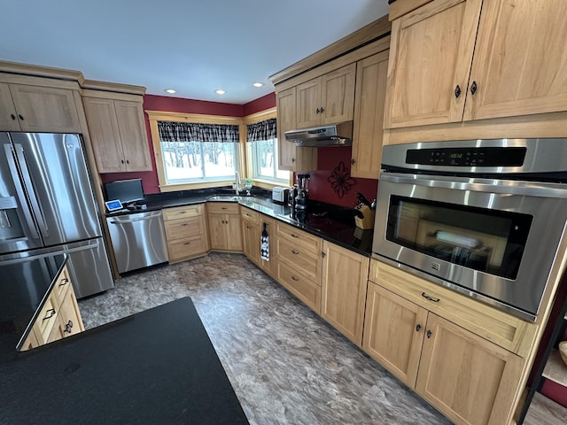 kitchen featuring dark countertops, stainless steel appliances, under cabinet range hood, light brown cabinets, and a sink