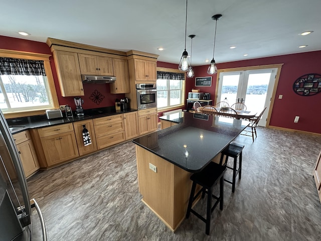 kitchen featuring under cabinet range hood, stainless steel oven, a kitchen breakfast bar, a center island with sink, and pendant lighting