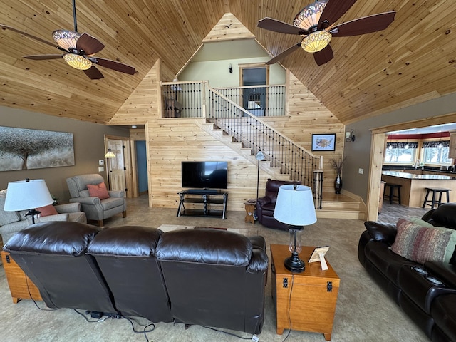 carpeted living area with stairway, a ceiling fan, wooden walls, high vaulted ceiling, and wooden ceiling