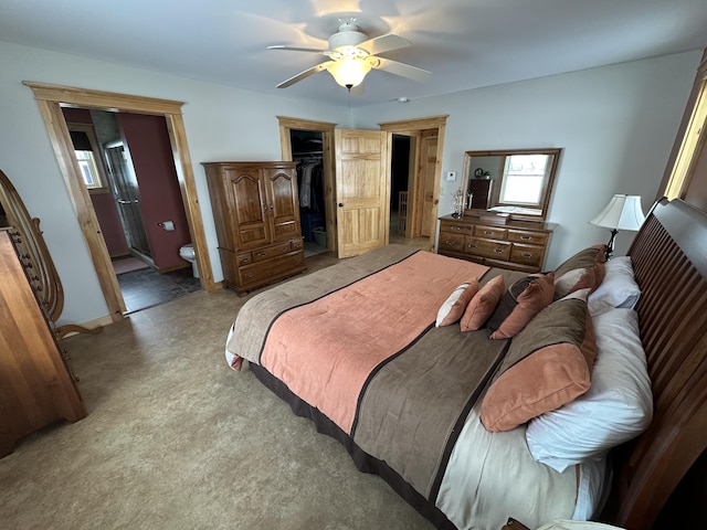 carpeted bedroom with ensuite bath, a closet, a walk in closet, and a ceiling fan