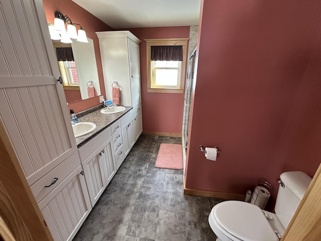 full bath featuring toilet, a sink, baseboards, double vanity, and a stall shower