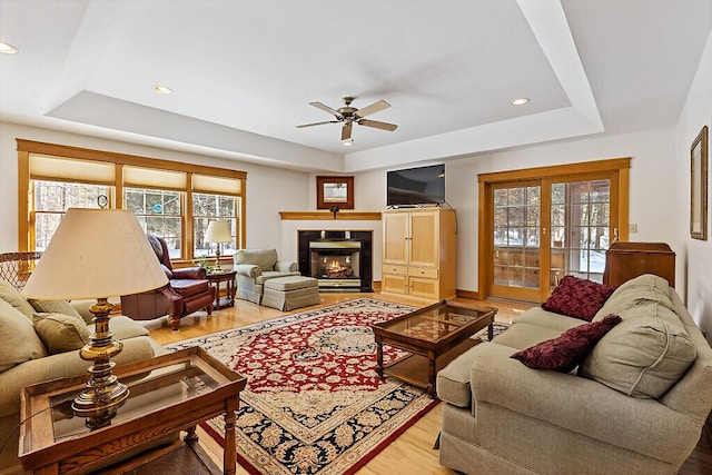 living area featuring a tile fireplace, a raised ceiling, light wood-style flooring, and recessed lighting