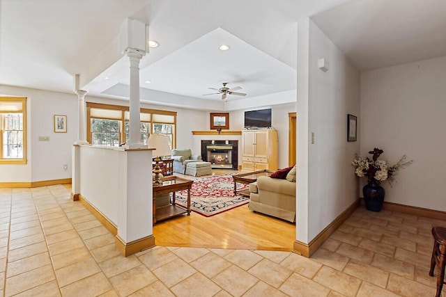 living area featuring decorative columns, recessed lighting, a ceiling fan, a glass covered fireplace, and baseboards