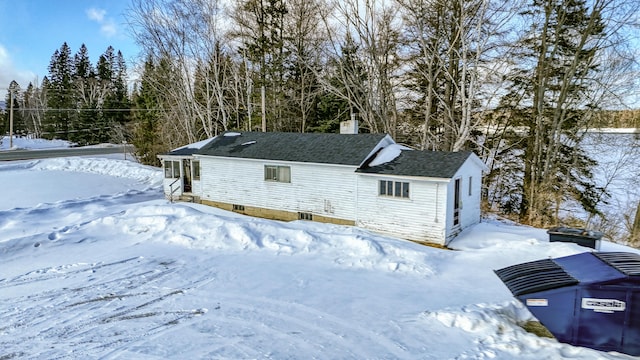 snow covered back of property with a shingled roof and a chimney