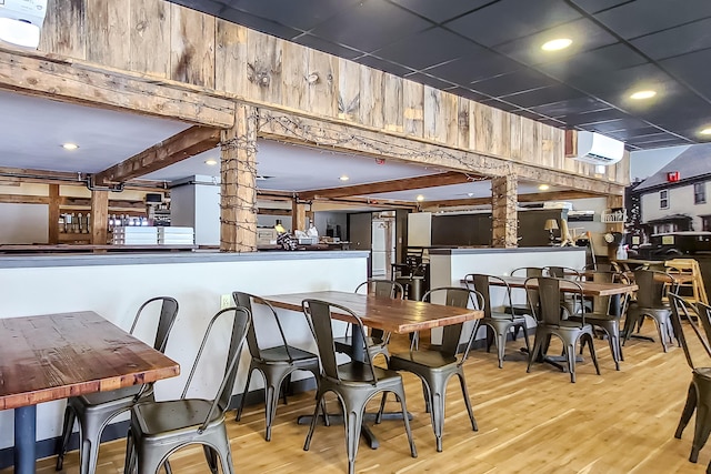 dining space with beam ceiling, a wall mounted AC, wood finished floors, a drop ceiling, and ornate columns