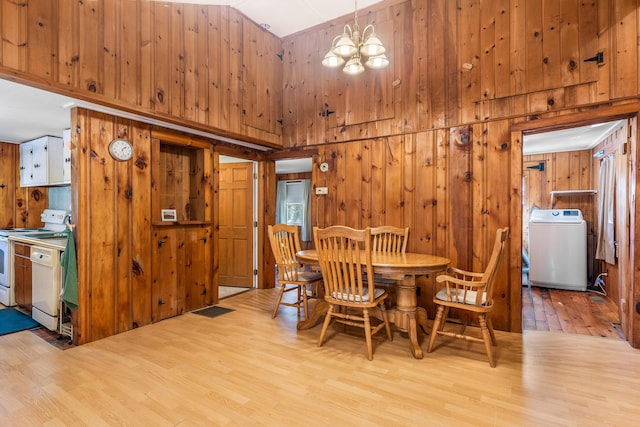 dining room with washer / dryer, light wood-type flooring, wood walls, and high vaulted ceiling