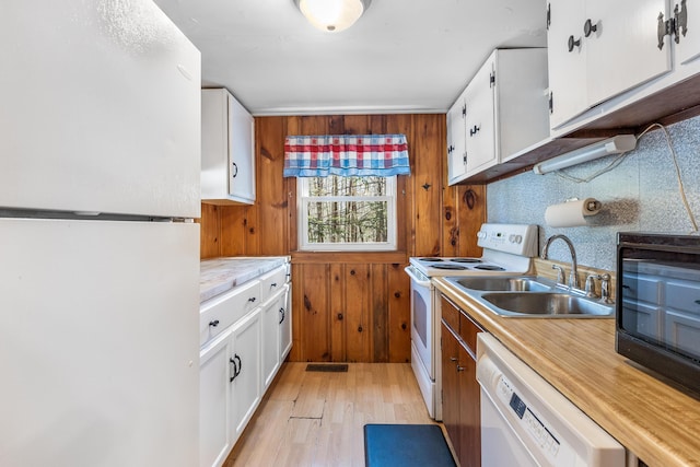 kitchen featuring light wood finished floors, light countertops, white appliances, white cabinetry, and a sink