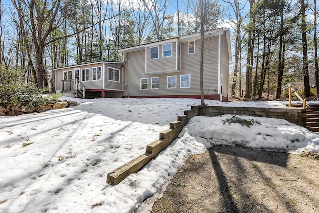 snow covered back of property featuring a sunroom