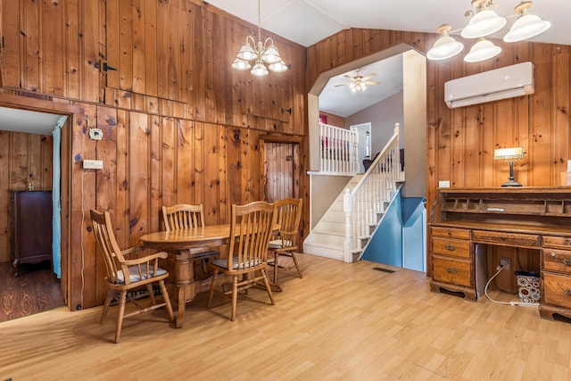 dining space with stairway, wood walls, an AC wall unit, lofted ceiling, and wood finished floors