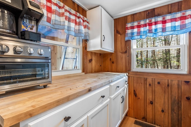 kitchen with white cabinetry, wooden walls, a healthy amount of sunlight, and wooden counters