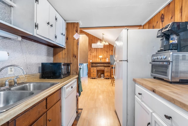 kitchen featuring wooden walls, vaulted ceiling, white appliances, white cabinetry, and a sink