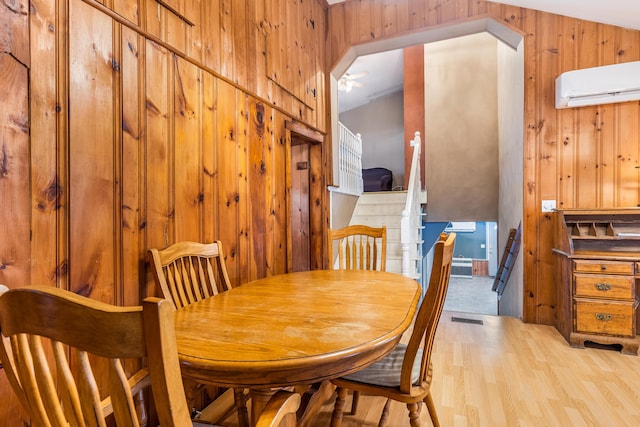 dining space featuring visible vents, wood walls, light wood-style floors, and a wall unit AC