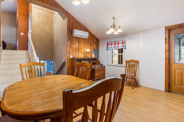 dining area featuring a wall unit AC, light wood finished floors, an inviting chandelier, vaulted ceiling, and wood walls