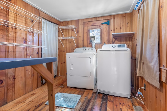 laundry area with visible vents, wood-type flooring, wood walls, laundry area, and washing machine and clothes dryer