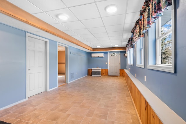 interior space with a wall unit AC, heating unit, visible vents, baseboards, and a drop ceiling