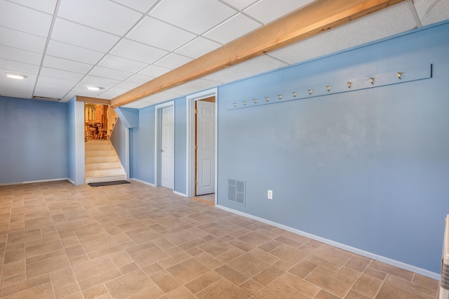 finished basement with stairs, baseboards, visible vents, and a paneled ceiling