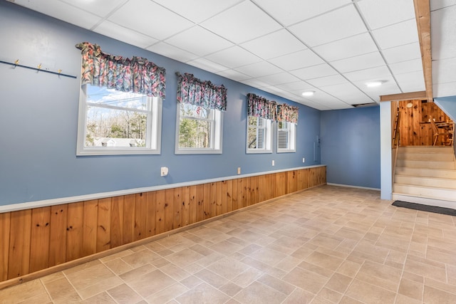 unfurnished room featuring stairway, wood walls, and a drop ceiling