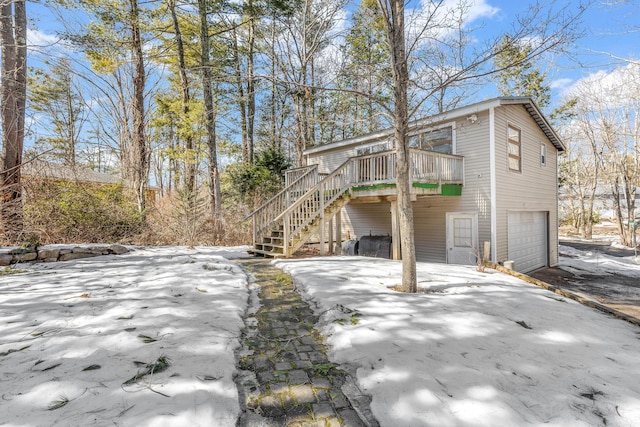 view of snowy exterior featuring stairway, a garage, a deck, and driveway