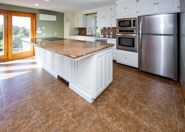 kitchen with a wall unit AC, backsplash, appliances with stainless steel finishes, white cabinetry, and a sink