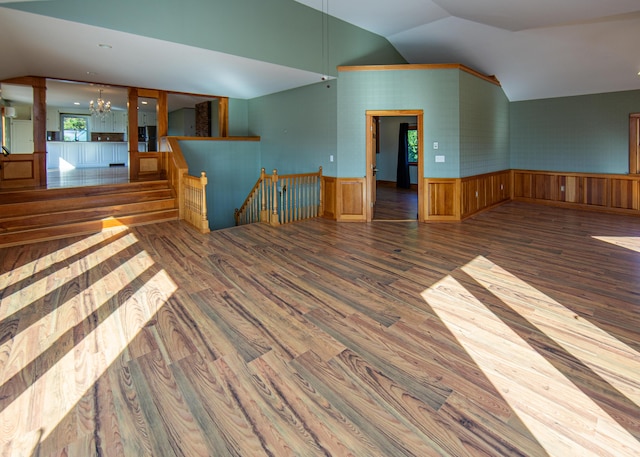 empty room featuring vaulted ceiling, wainscoting, wood finished floors, and an inviting chandelier